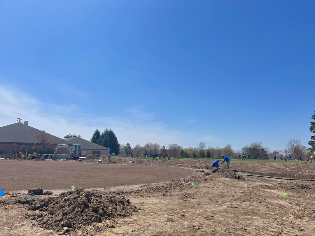 Construction workers preparing land for development under a clear blue sky.